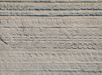Grey sand with traces of bicycle treads in the rays of the setting sun. Background with abstract...