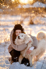 A girl walks with her beloved pet Samoyed in winter on the shore of a lake in the park.