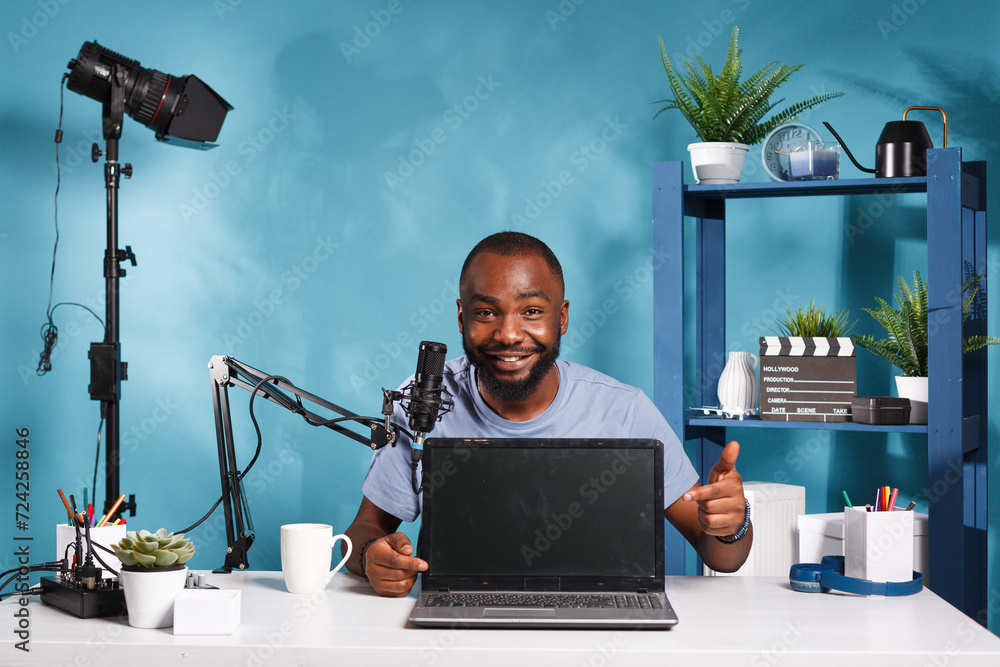 Poster smiling streamer announcing giveaway and pointing at laptop gift while recording video for online bl