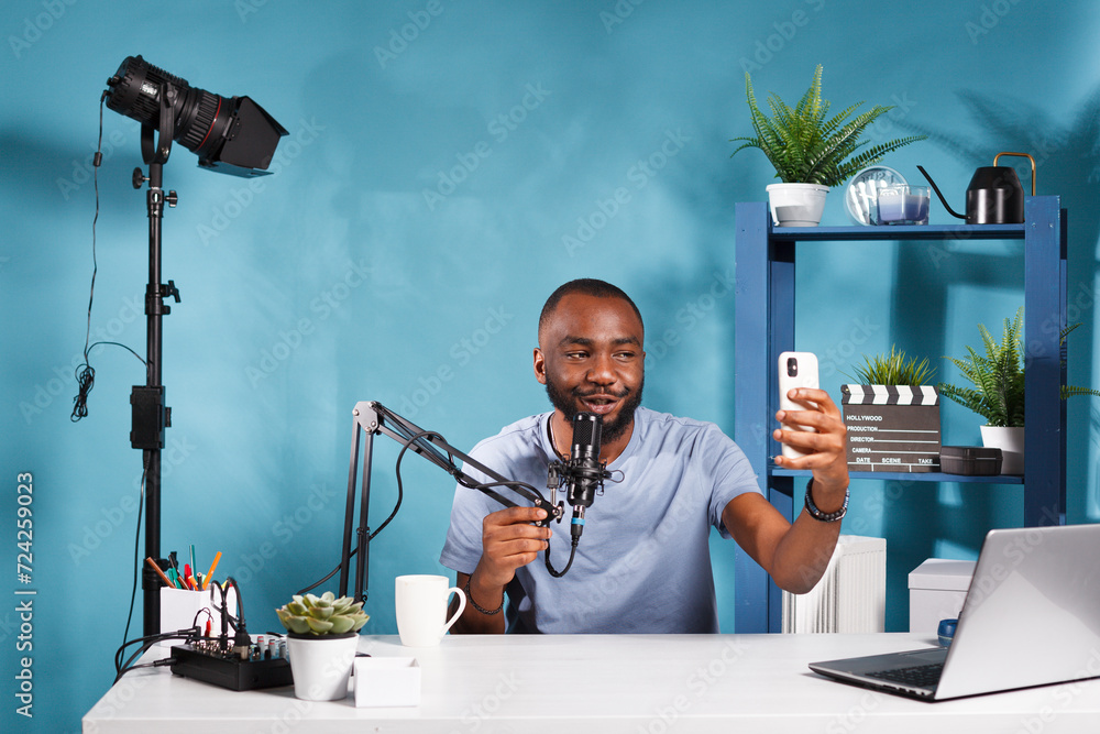 Poster african american vlogger holding smartphone and speaking in microphone while creating web content. y