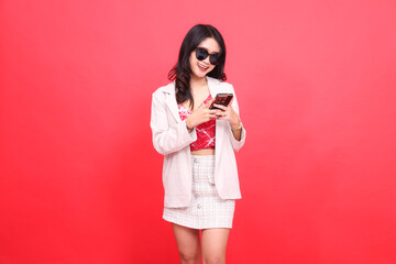 A beautiful Asian Indonesian woman wearing glasses, cheerfully slanted to the left, operates a cellphone cheerfully wearing a cream-colored blazer