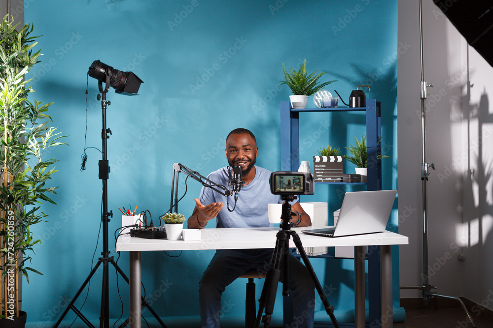 Poster african american blogger using camera for web streaming in professional studio. smiling young man vl