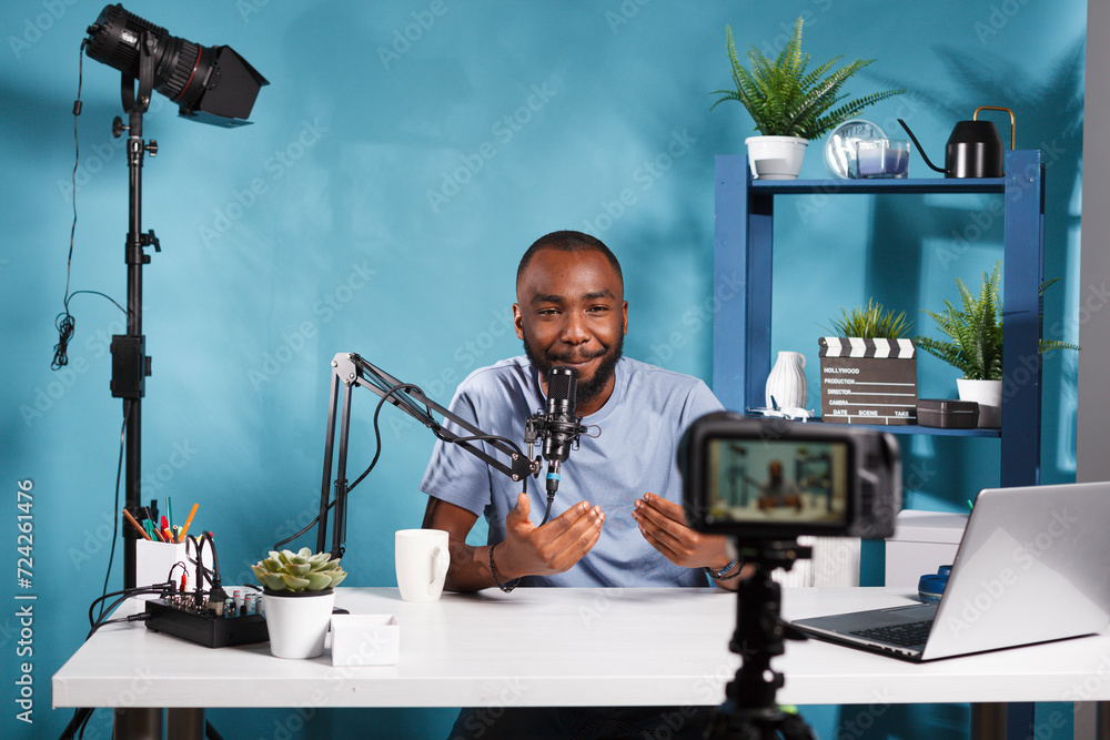 Poster african american blogger creating professional video content with camera while streaming in studio. 