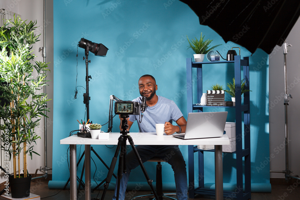 Poster smiling vlogger recording video and looking at professional camera while working in studio. cheerful