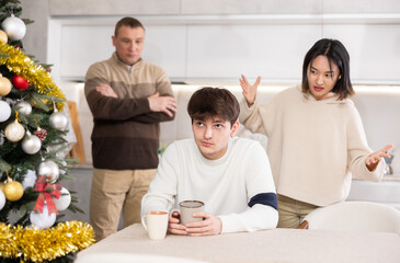 Domestic quarrel during Christmas celebration - father and sister scolding young guy in home kitchen