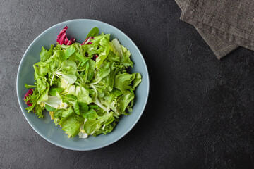 Green salad leaves in bowl on black table.