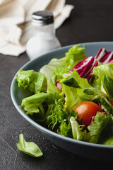 Green salad leaves in bowl on black table.