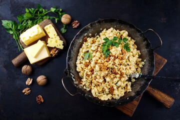 Traditionelle Allgäuer Käsespätzle mit Walnüssen serviert als Draufsicht in einer gusseisernen Bratpfanne auf einem rustikalen Board 