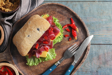 Delicious sandwich with bresaola, lettuce and cheese served on light blue wooden table, flat lay