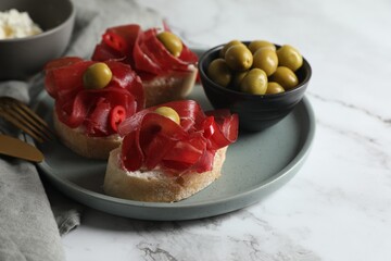 Delicious sandwiches with bresaola, cream cheese and olives served on white marble table, closeup