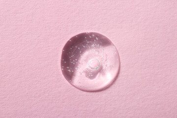 Drop of cosmetic serum on pink background, top view