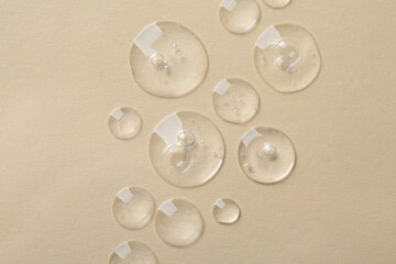 Drops of cosmetic serum on beige background, top view
