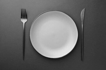 Empty plate, fork and knife on grey table, top view