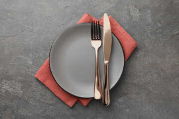 Clean plate, cutlery and napkin on grey textured table, top view