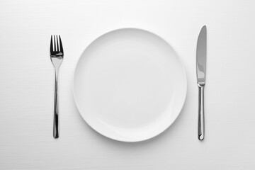 Empty plate, fork and knife on white table, top view