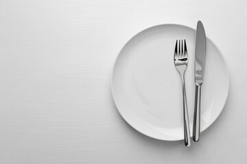 Clean plate, fork and knife on white table, top view. Space for text
