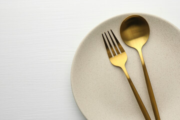 Clean plate, fork and spoon on white table, top view. Space for text