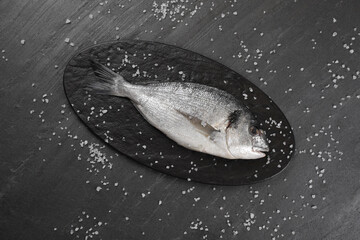 Fresh raw dorado fish and sea salt on black table, flat lay