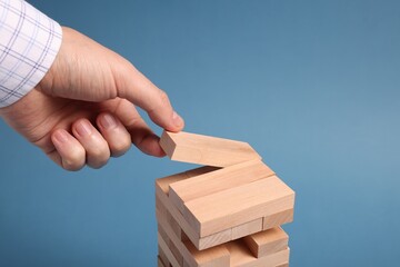Playing Jenga. Man building tower with wooden blocks on blue background, closeup
