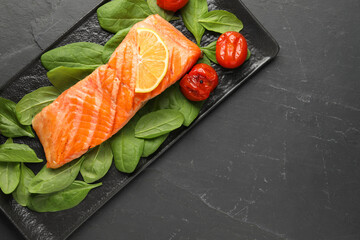 Tasty grilled salmon with tomatoes, spinach and lemon on black table, top view. Space for text