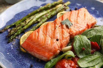 Tasty grilled salmon with tomatoes, asparagus, spinach and spices on plate, closeup