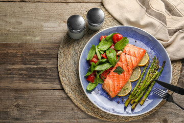 Tasty grilled salmon with tomatoes, asparagus, spinach and lemon served on wooden table, flat lay. Space for text