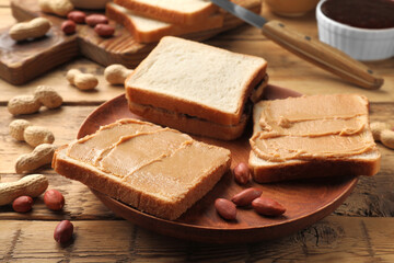 Tasty peanut butter sandwiches and peanuts on wooden table, closeup