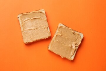Tasty peanut butter sandwiches on orange background, flat lay