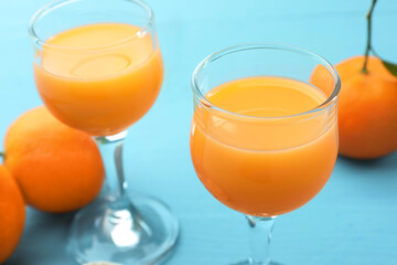 Delicious tangerine liqueur and fresh fruits on light blue table, closeup