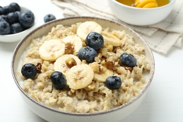 Tasty oatmeal with banana, blueberries, walnuts and honey served in bowl on white wooden table, closeup