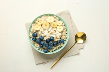 Tasty oatmeal with banana, blueberries, coconut flakes and honey served in bowl on beige table, top view