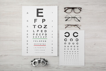 Vision test chart, glasses and trial frame on light wooden background, flat lay