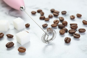 Pink milk frother wand, sugar cubes and coffee beans on white marble table, closeup