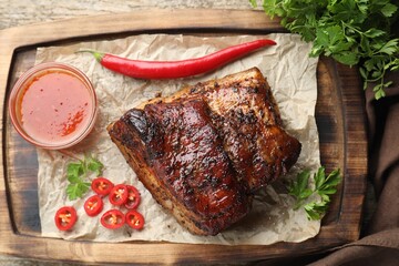 Piece of baked pork belly served with sauce and chili pepper on wooden table, top view