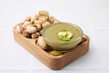 Tasty pistachio cream in bowl and nuts on white tiled table, closeup
