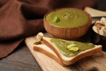 Toasts with tasty pistachio cream and nuts on wooden table, closeup. Space for text