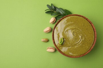 Tasty pistachio cream in bowl, leaves and nuts on green background, top view. Space for text