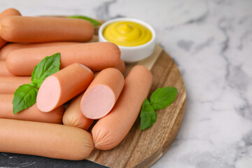 Delicious boiled sausages and basil on white marble table, closeup