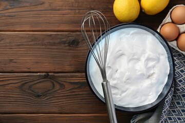 Bowl with whipped cream, whisk and ingredients on wooden table, flat lay. Space for text