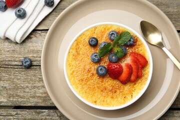 Delicious creme brulee with berries and mint in bowl on wooden table, top view