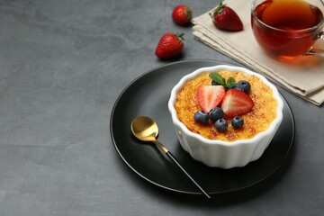 Delicious creme brulee with berries and mint in bowl on grey table. Space for text
