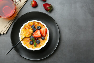 Delicious creme brulee with berries and mint in bowl served on grey table, flat lay. Space for text