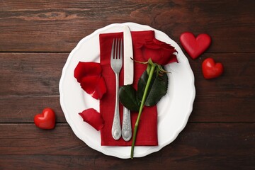 Romantic place setting with red rose and decorative hearts on wooden table, top view. St....