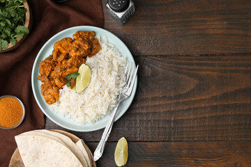 Delicious chicken curry with rice and ingredients on wooden table, flat lay. Space for text