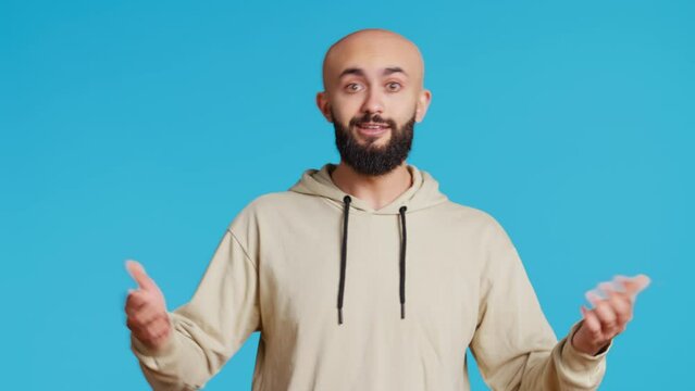 Middle eastern guy pointing down to show something, trying to explain by looking down at his feet. Arab person using index fingers to point downwards on blue background. Camera 2.