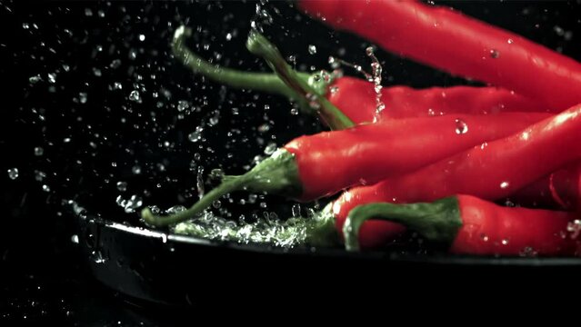 The chili peppers fall with splashes into the plate. On a black background. Filmed on a high-speed camera at 1000 fps. High quality FullHD footage