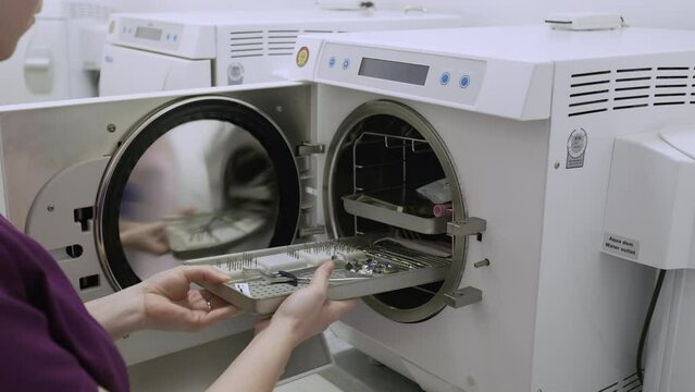 Woman takes out sterilized dental tools from autoclave chamber. Sterilization practice in dentistry protects patients and professionals against infection