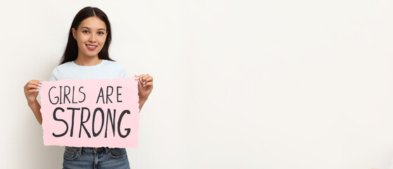 Young woman holding paper with slogan GIRLS ARE STRONG on white background with space for text....