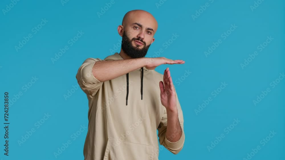 Poster middle eastern person doing timeout gesture on camera, asking for a break to stop working over blue 
