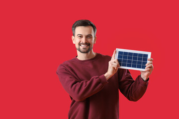 Handsome man with portable solar panel on red background